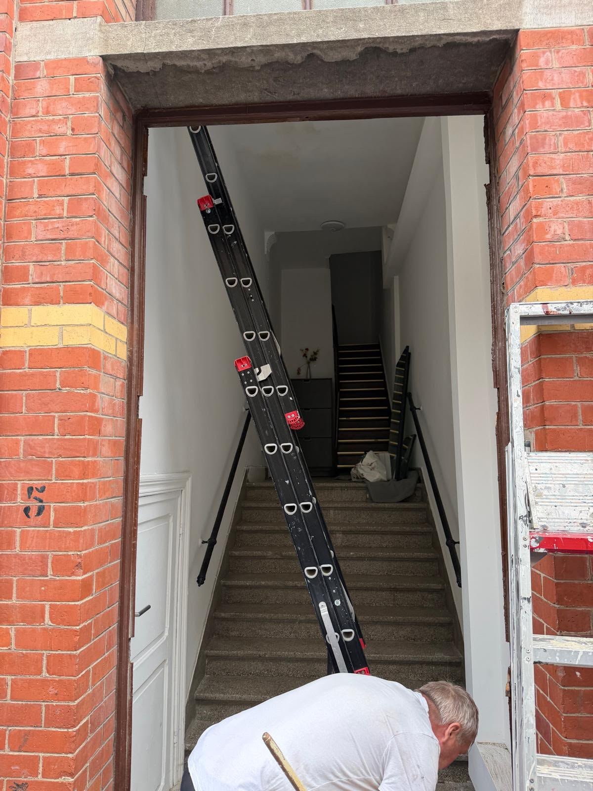 Porte d'entrée d'un immeuble en briques avec échelle dans le couloir et ouvrier au travail