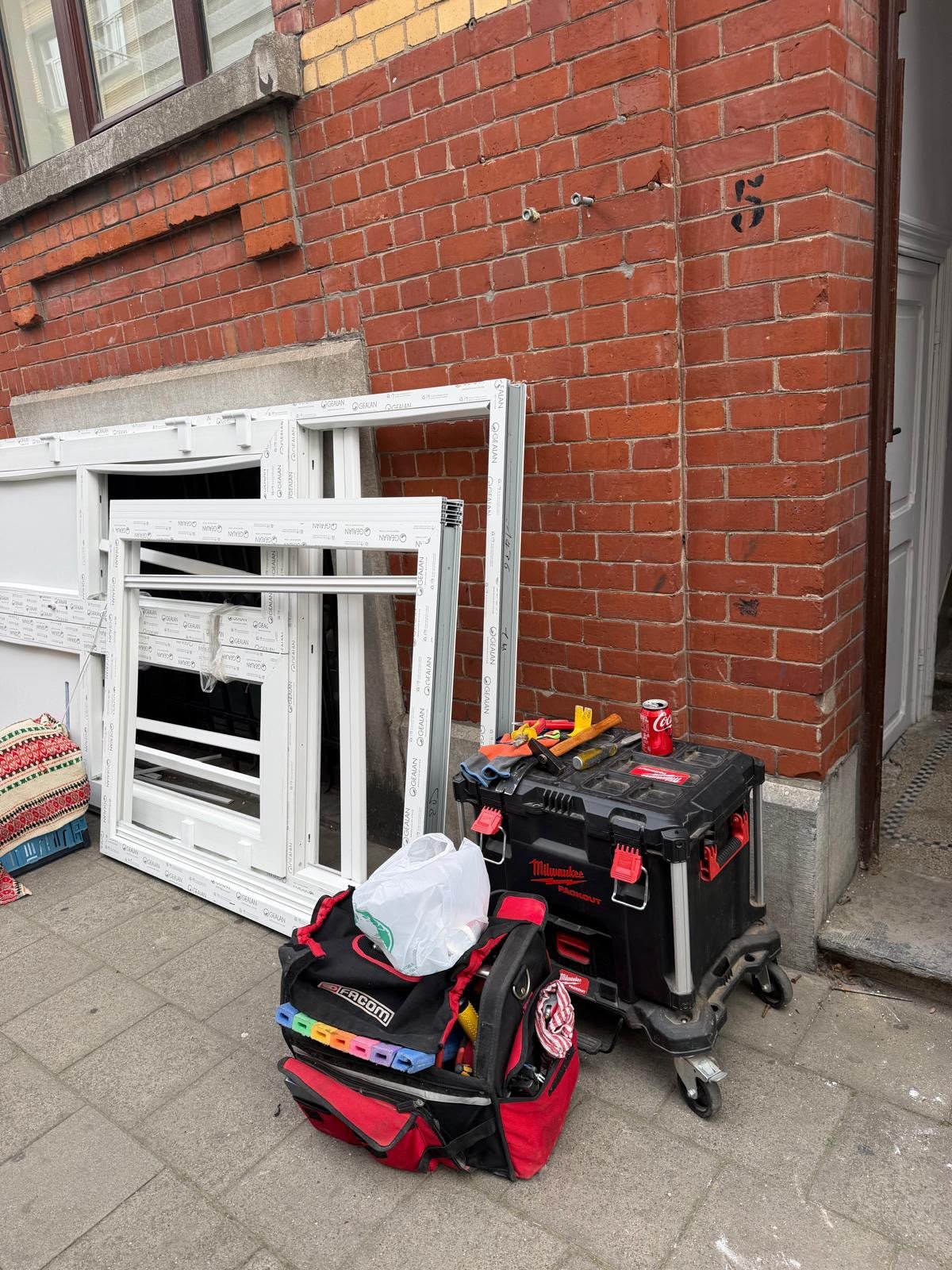 Matériel de serrurier et châssis déposés au pied d'une façade en briques