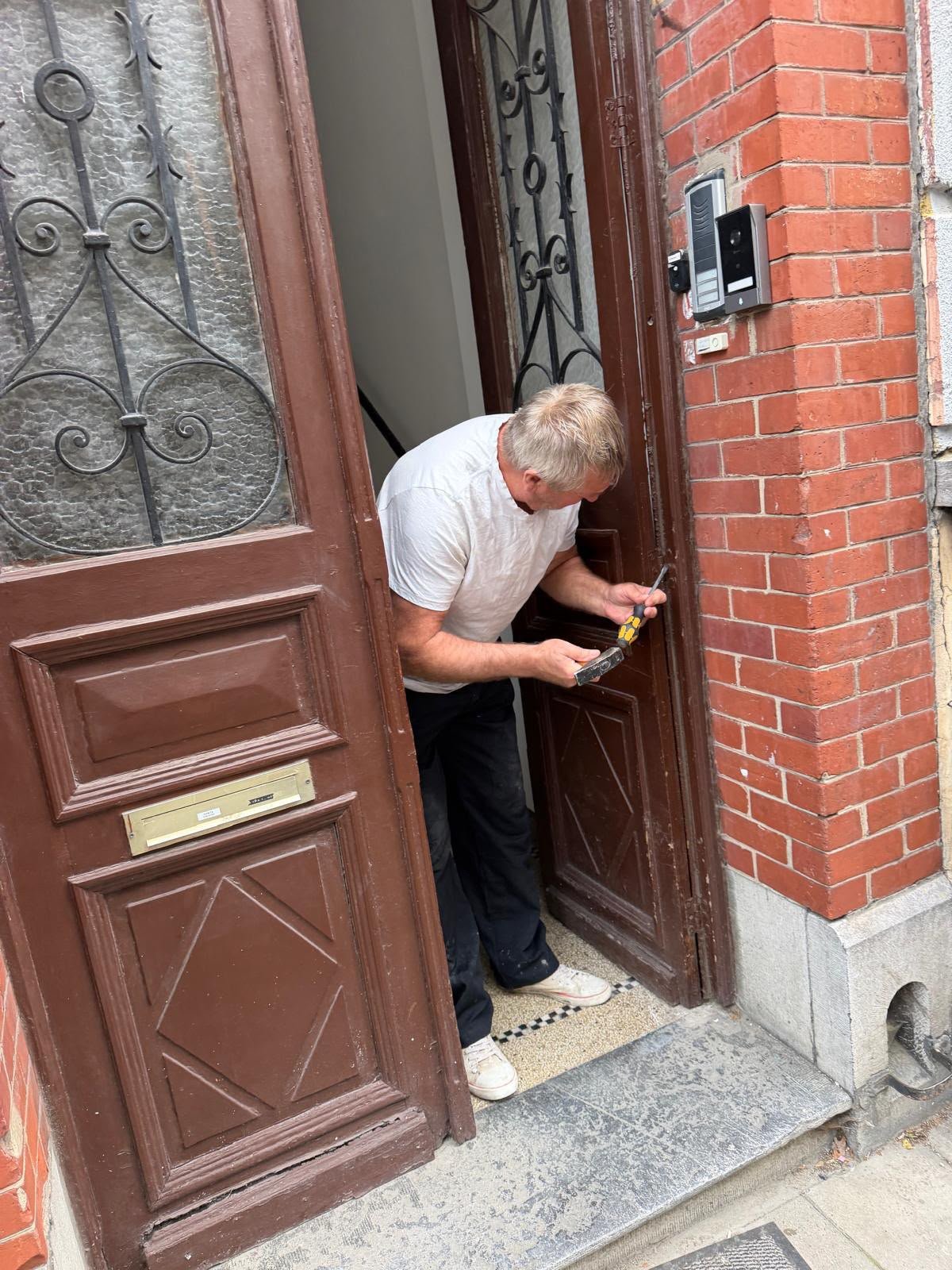 Serrurier intervenant sur une porte d'entrée ancienne en bois d'un immeuble en briques