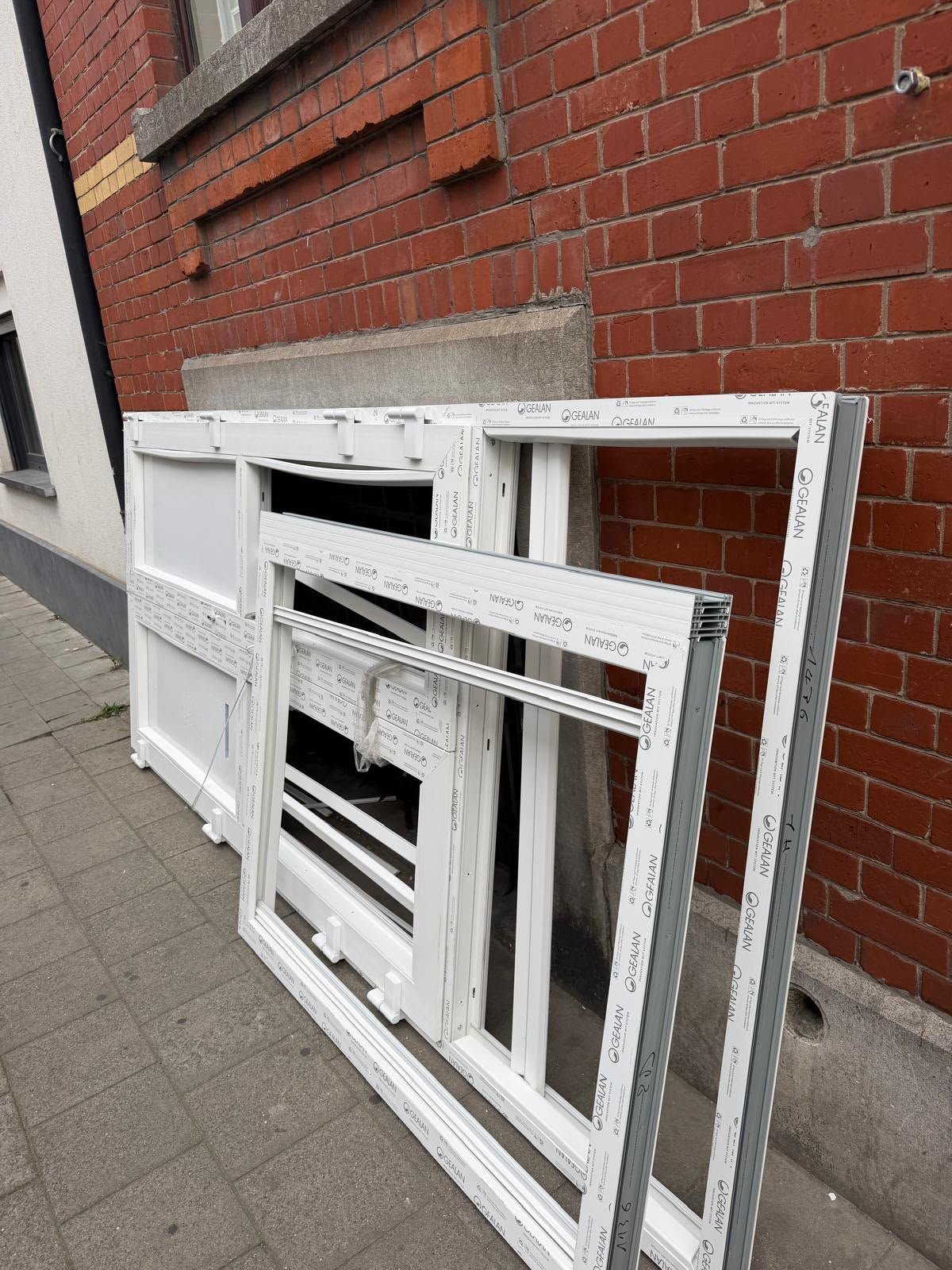 Anciens châssis blancs déposés contre une façade en briques lors d'un chantier de porte