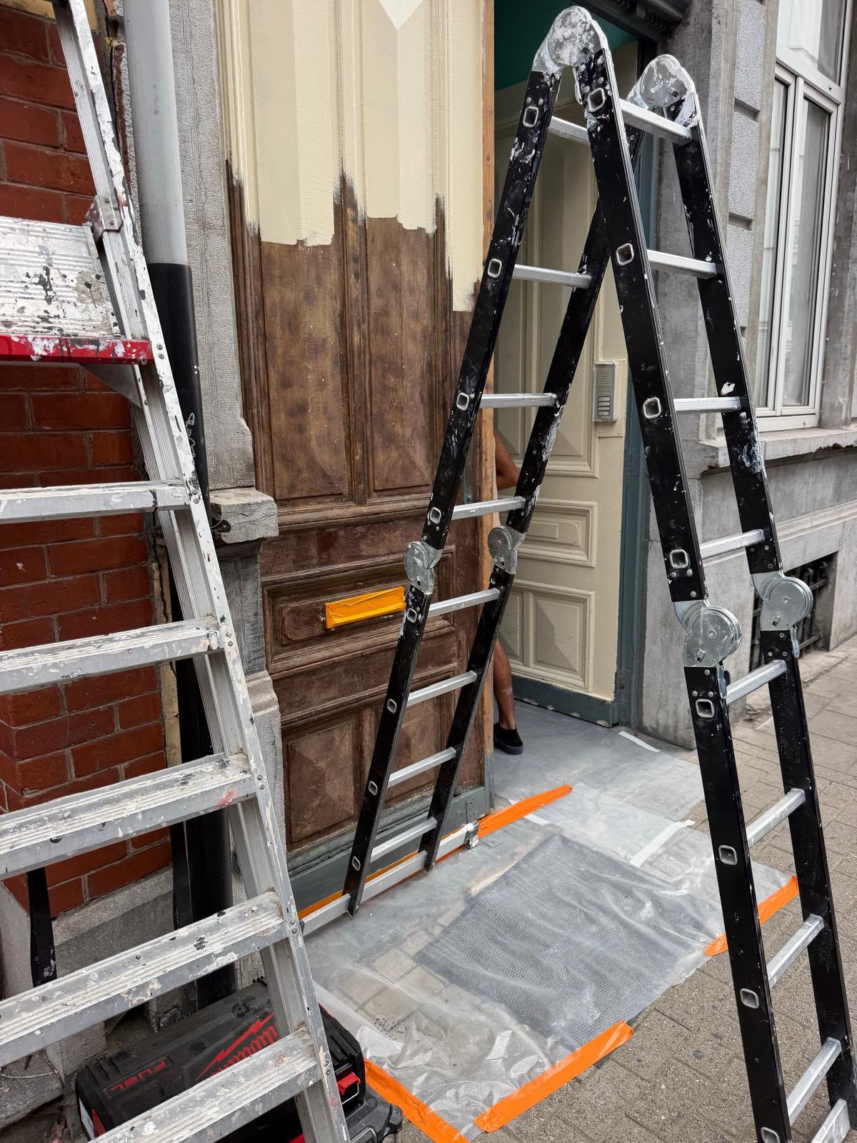 Porte d'entrée en bois en cours de rénovation avec échelles devant l'immeuble